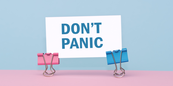 a piece of white paper with the words 'DON'T PANIC' printed in blue text, the paper is held up by 2 coloured foldback paper grips against a pink and blue background. 