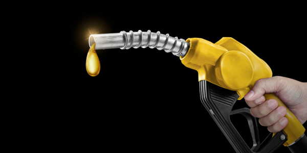 A person holding a fuel pump nozzle, the end of the nozzle is dripping with liquid gold. 