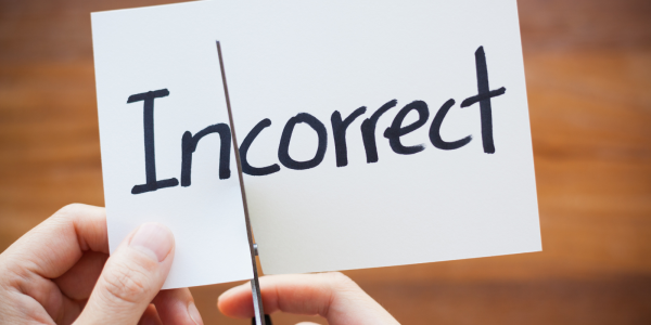 A piece of paper with the word 'INCORRECT' written in black ink, the paper is being cut with scissors in between 'IN' and 'CORRECT' 