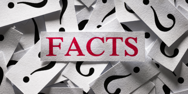 Lots of pieces of paper with question marks printed on them all bundled in a pile, on the top of the pile is a larger piece of paper with the word 'FACTS' on it in red text. 