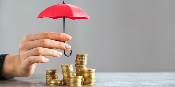 Stacks of coins with a person holding an umbrella above. 