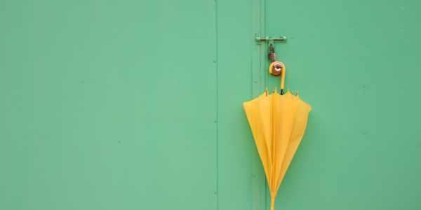 A yellow umbrella hanging on a doorknob against a pale green background. 