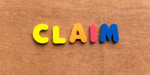small colourful plastic letters arranged to spell out the word 'CLAIM' against a wooden background. 