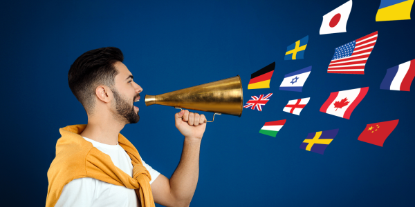 A person holding a cone to their mouth with various international flags floating out of the cone. 