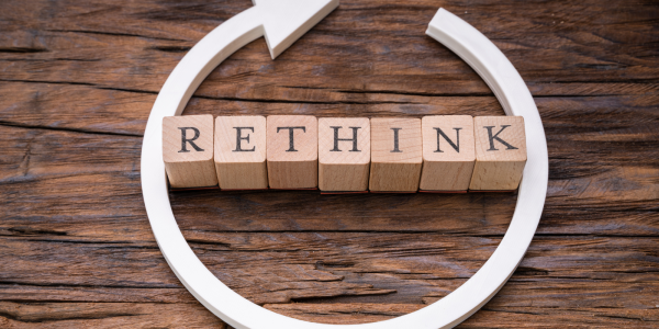 Wooden letters spelling out the word 'RETHINK' with a white circular arrow around it. 