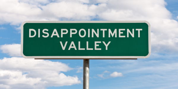 A green road sign with the words 'DISAPPOINTMENT VALLEY' in white text.