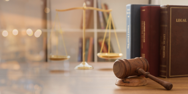 brass scales, a hammer and gavel and legal books can be seen on a desk.