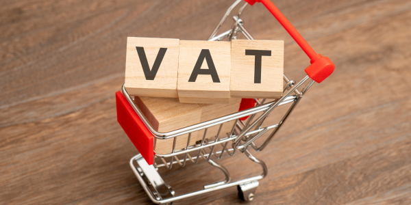 tiny shopping trolley with wooden lettered blocks inside, together they spell out the word 'VAT'. 