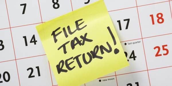 a wall calendar with a yellow post it note stuck to it, the note reads 'FILE TAX RETURN' 