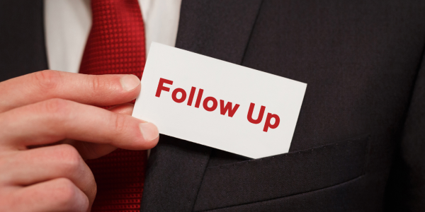 A person pulling a small card from their pocket, the card reads 'FOLLOW UP' in red text.