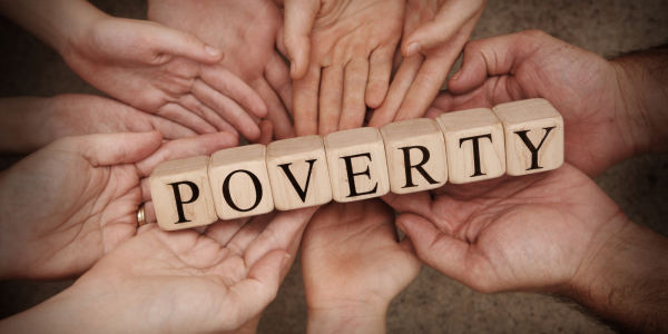 Various hands holding wooden lettered blocks which spell out the word 'POVERTY'. 