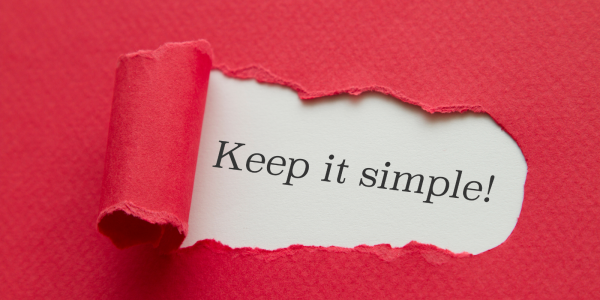 Red paper with a tear in the centre, through the tear the words 'KEEP IT SIMPLE!' can be seen typed onto a white paper.