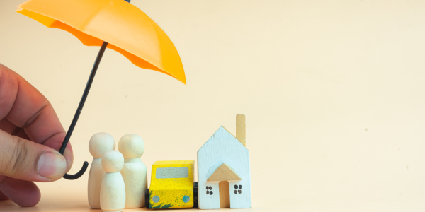 A small model home with a small family and car, a person is holding an umbrella above them. 