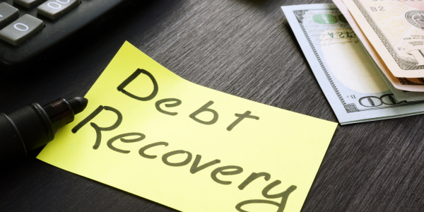 A yellow post it note with the words 'DEBY RECOVERY' written in it in black ink sat on a desk.