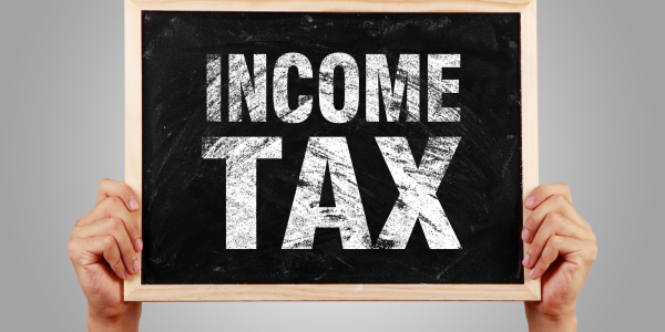 A person holding up a small chalkboard with the words 'INCOME TAX' written on it in white chalk. 