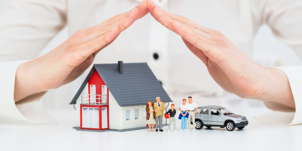 A person's hands covering a model home, car and tiny family to protect them.