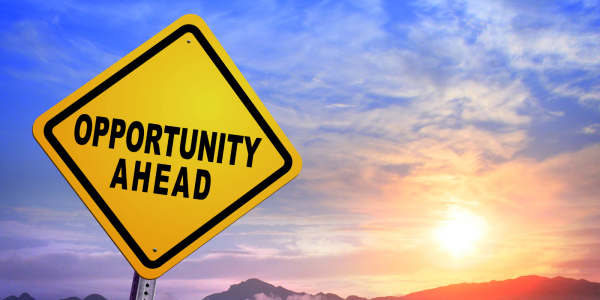 A yellow road sign with the words 'OPPORTUNITY AHEAD' in black text, a sunset can be seen in the background